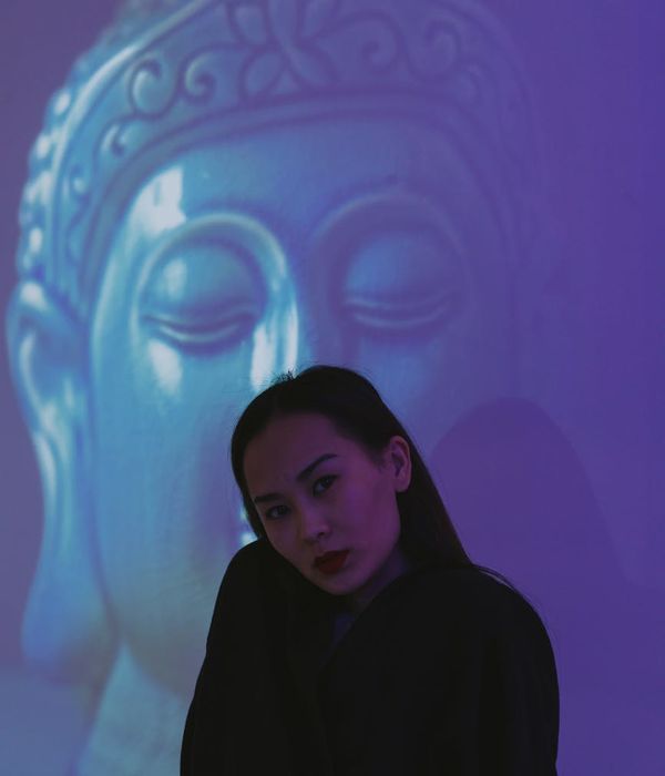 Woman in a calm yoga pose against a dark background with pink light accents.